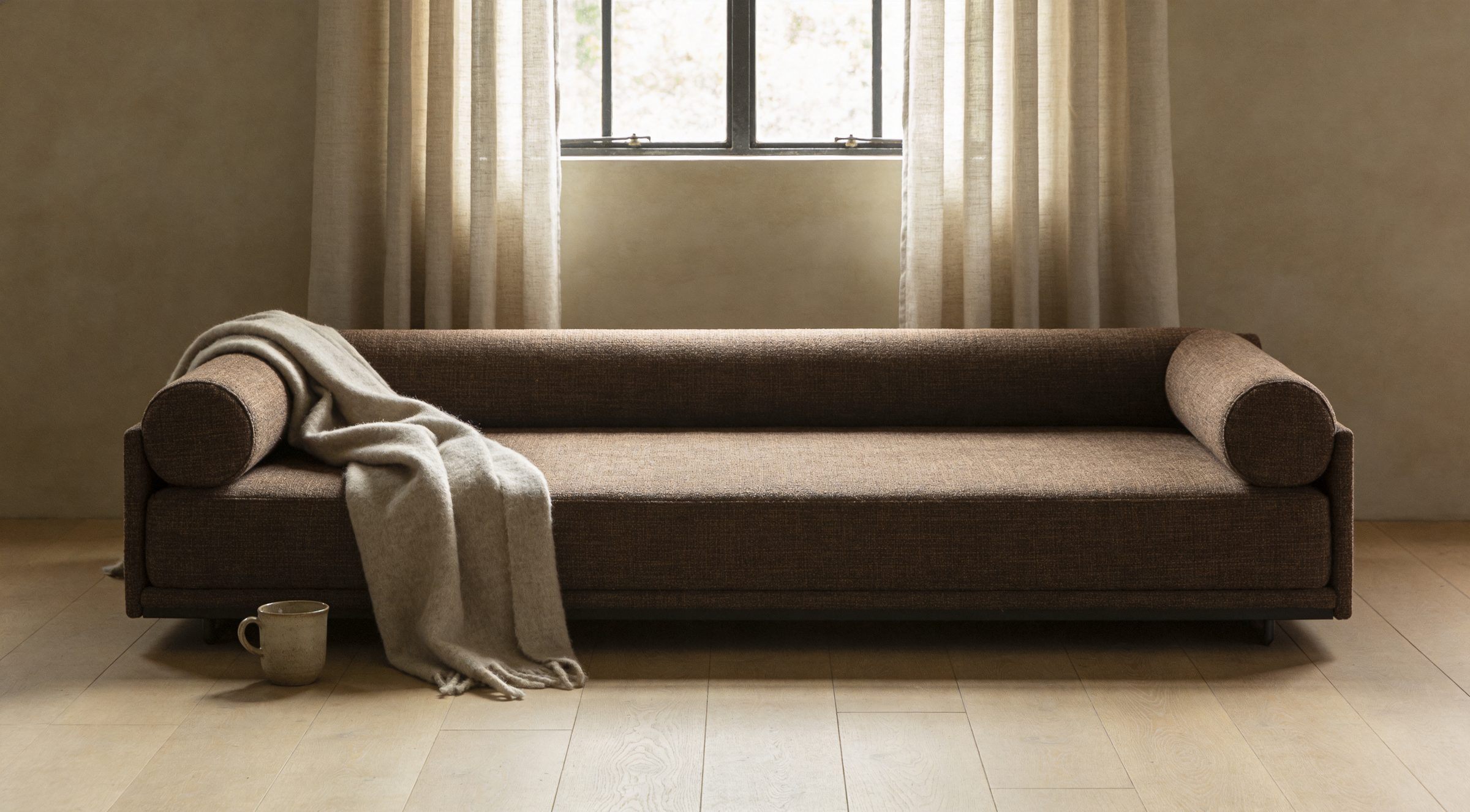 A long, low sofa with bolsters and a wool throw